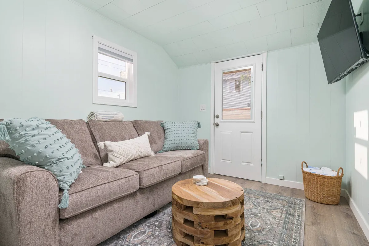 A bright, inviting living space featuring a comfortable sofa and a door leading outdoors. The room is styled for relaxation and socializing, with natural light hinting at easy indoor-outdoor transitions—perfect for guests who want to enjoy both the comforts of home and access to the yard.