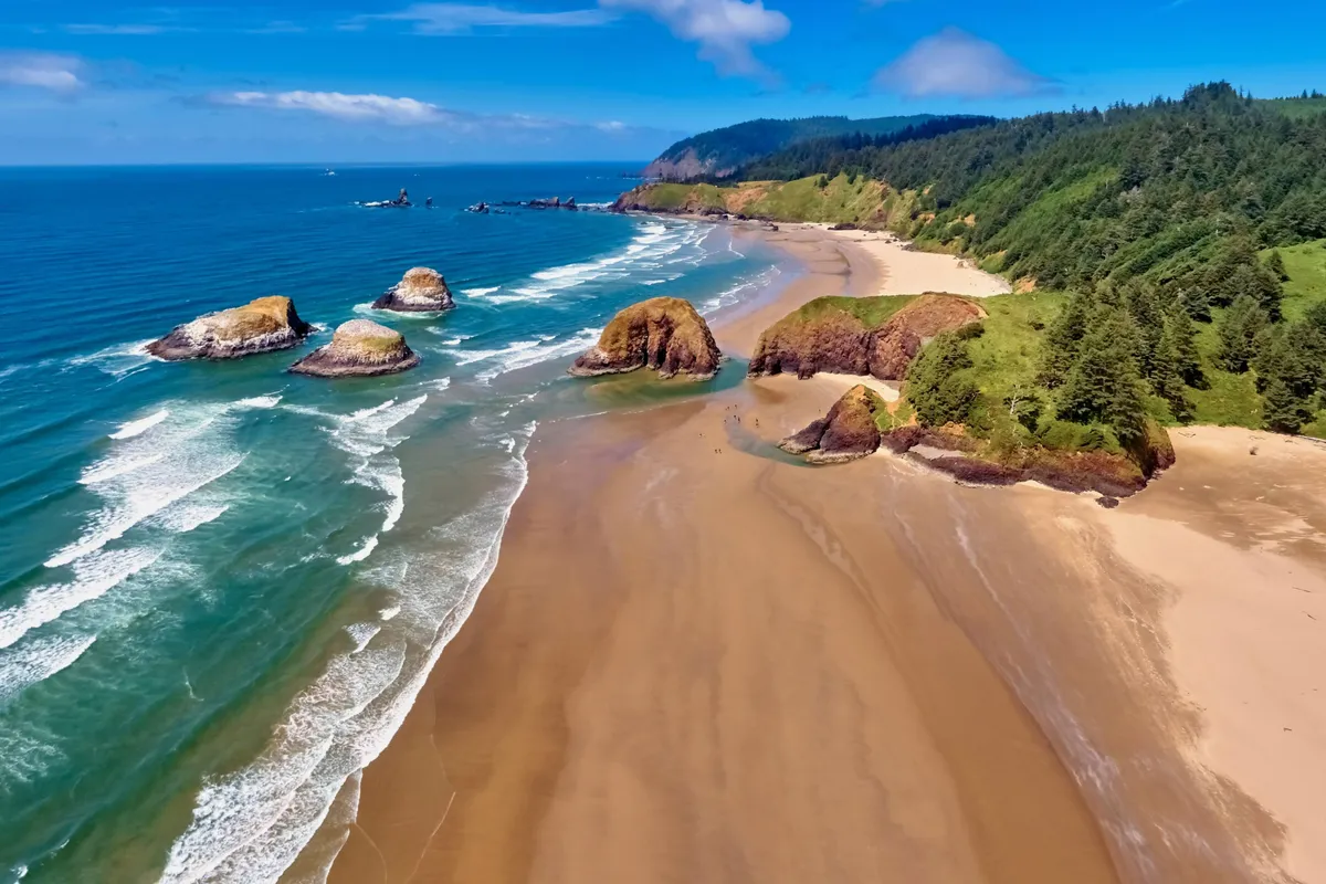 A panoramic view of the coastline with ocean waves, rock formations, sandy beach, and distant hills. The tranquil outdoor setting is perfect for imagining a soothing soak under the open sky, especially during sunset or stargazing moments referenced in the section.