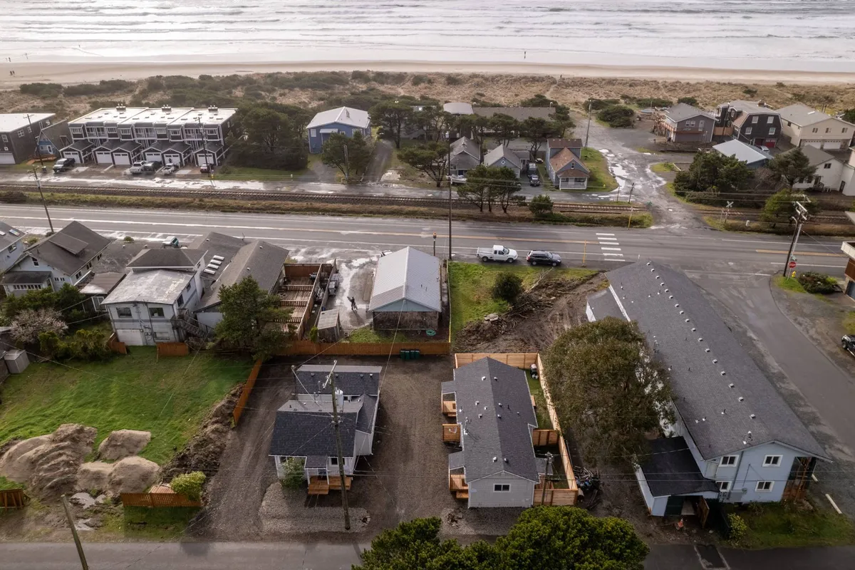 A tranquil exterior shot of beachfront homes nestled along a road with lush trees. The expansive sandy shoreline is visible, inviting residents and visitors to enjoy long beach walks, outdoor relaxation, and exploration. The scene reflects a peaceful yet lively coastal neighborhood ideal for gathering with friends or participating in local events.
